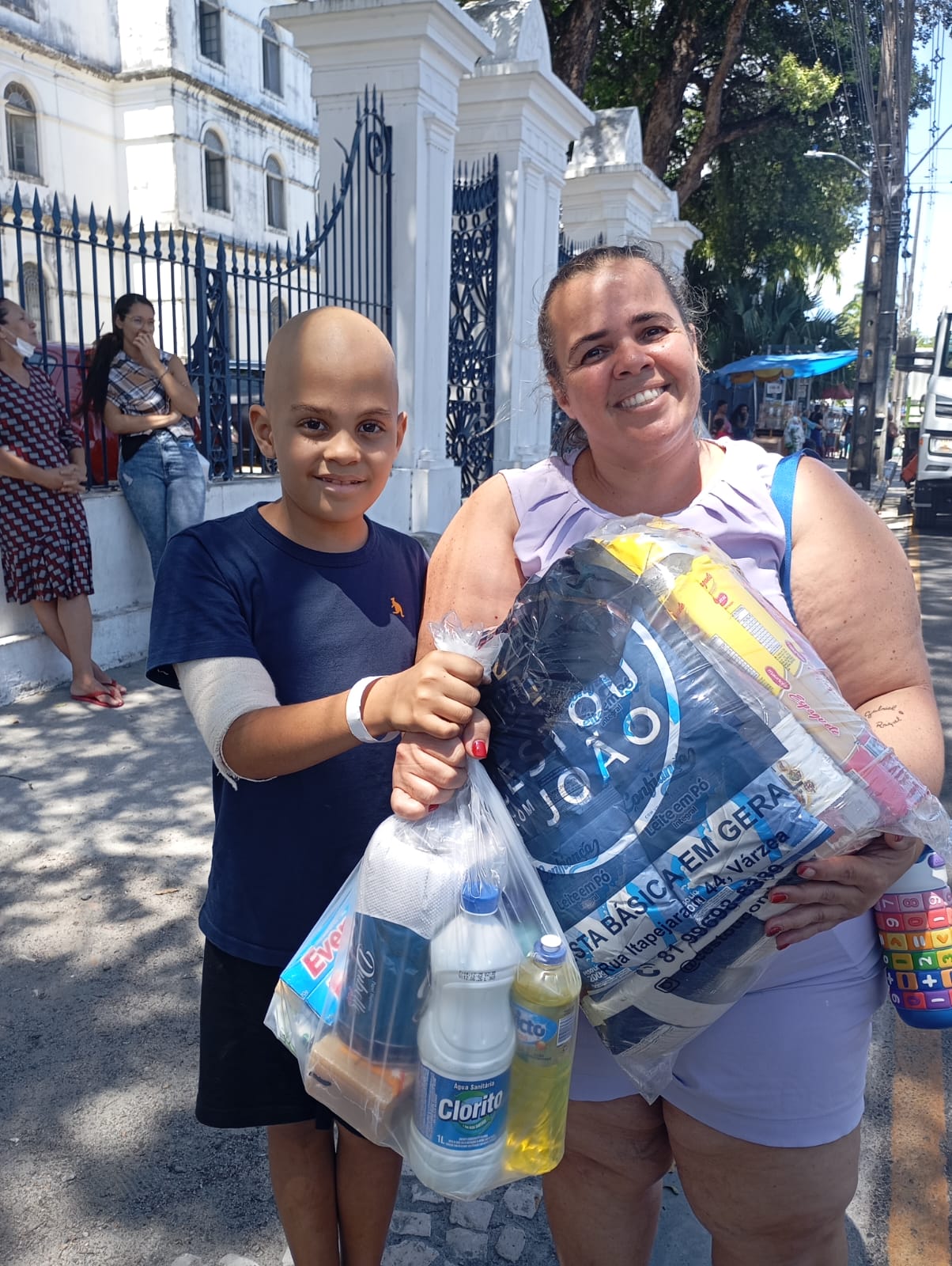 Mãe e filho em tratamento recebendo cesta básica entregue pela Por Amor de Muitos